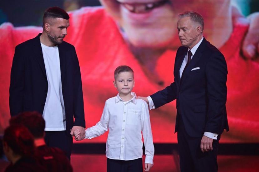 German TV host Johannes B. Kerner (R), cancer survivor Collin (C) and former German football player Lukas Podolski stand on stage during the charity gala "Ein Herz Für Kinder" (A heart for children) in Berlin, on December 6, 2025.  Sebastian Gollnow / POOL / AFP
