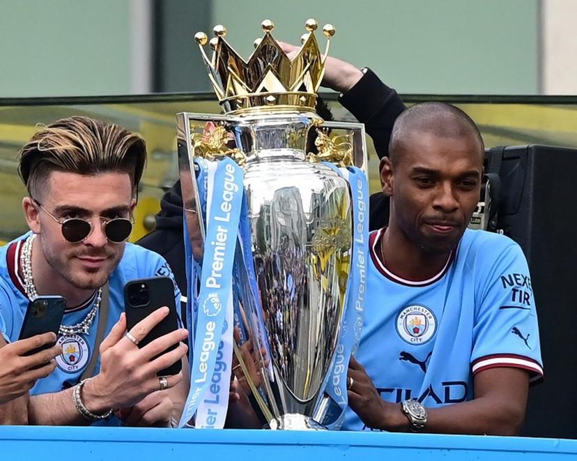 Manchester City's Brazilian midfielder Fernandinho (R) and Manchester City's English midfielder Jack Grealish (L) are seen with the trophy as Manchester City's players begin an open-top bus parade through the streets of Manchester in north-west England on May 23, 2022, to celebrate winning the 2021-22 Premier League title. Manchester City's latest Premier League title triumph established the champions as a burgeoning dynasty. City's fourth title in five seasons is arguably the greatest achievement of Guardiola's glittering career as he found a way to hold off Liverpool's relentless challenge by one point.  Paul ELLIS / AFP