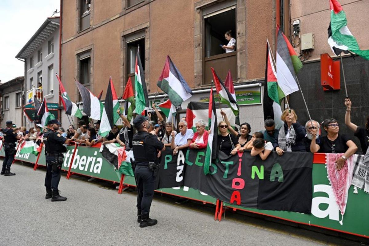 Police officers stand as Pro-Palestinian demonstrators wave Palestinian flags at the finish line of the 12th stage of the Vuelta a Espana, a 144,9 km race between Laredo and Corrales de Buelna, on September 4, 2025.   ANDER GILLENEA / AFP