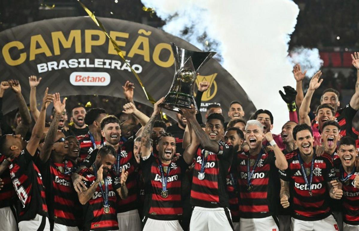 Flamengo's Uruguayan midfielder #10 Giorgian de Arrascaeta (C-L) and forward #27 Bruno Henrique (C-R) lift the Brasileirao trophy after winning the Brasileirao Serie A football match between Flamengo and Ceara at Maracana Stadium in Rio de Janeiro, Brazil, on December 3, 2025.  Mauro PIMENTEL / AFP