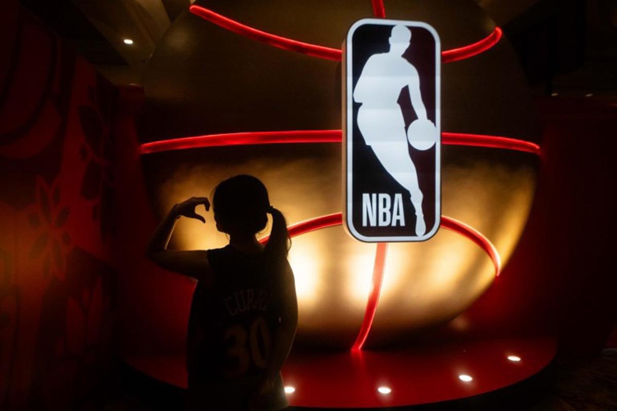 A fan poses next to the National Basketball Association logo before the NBA pre-season basketball game between the Phoenix Suns and Brooklyn Nets at the Venetian Arena in Macau on October 12, 2025.  Eduardo Leal / AFP