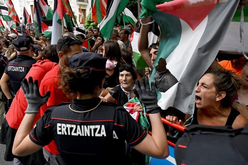 Pro-Palestinian protesters holding Palestinian flags shout as Basque regional police 'Ertzaintza' officers stand during the eleventh stage of the Vuelta a Espana cycling tour, a 167 km race from Bilbao to Bilbao, on September 3, 2025.  ANDER GILLENEA / AFP