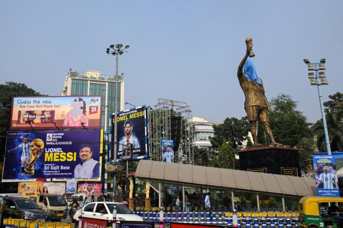 Commuters cross promotional posters and veiled statue of Inter Miami's Argentine forward #10 Lionel Messi, on the eve of his visit, in Kolkata on December 12, 2025. Lionel Messi will unveil a 70-foot statue of himself in India on December 13 as he embarks on a three-day trip of the country that has sparked a fan frenzy.  Dibyangshu SARKAR / AFP