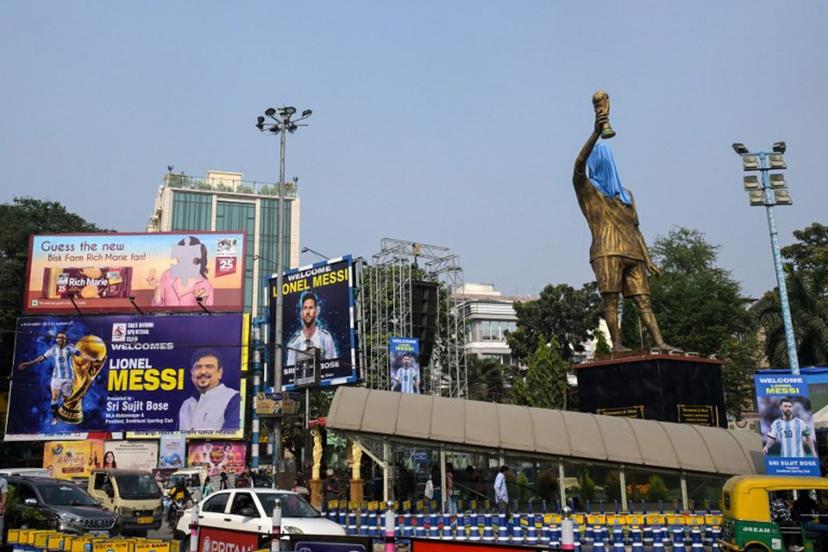 Commuters cross promotional posters and veiled statue of Inter Miami's Argentine forward #10 Lionel Messi, on the eve of his visit, in Kolkata on December 12, 2025. Lionel Messi will unveil a 70-foot statue of himself in India on December 13 as he embarks on a three-day trip of the country that has sparked a fan frenzy.  Dibyangshu SARKAR / AFP