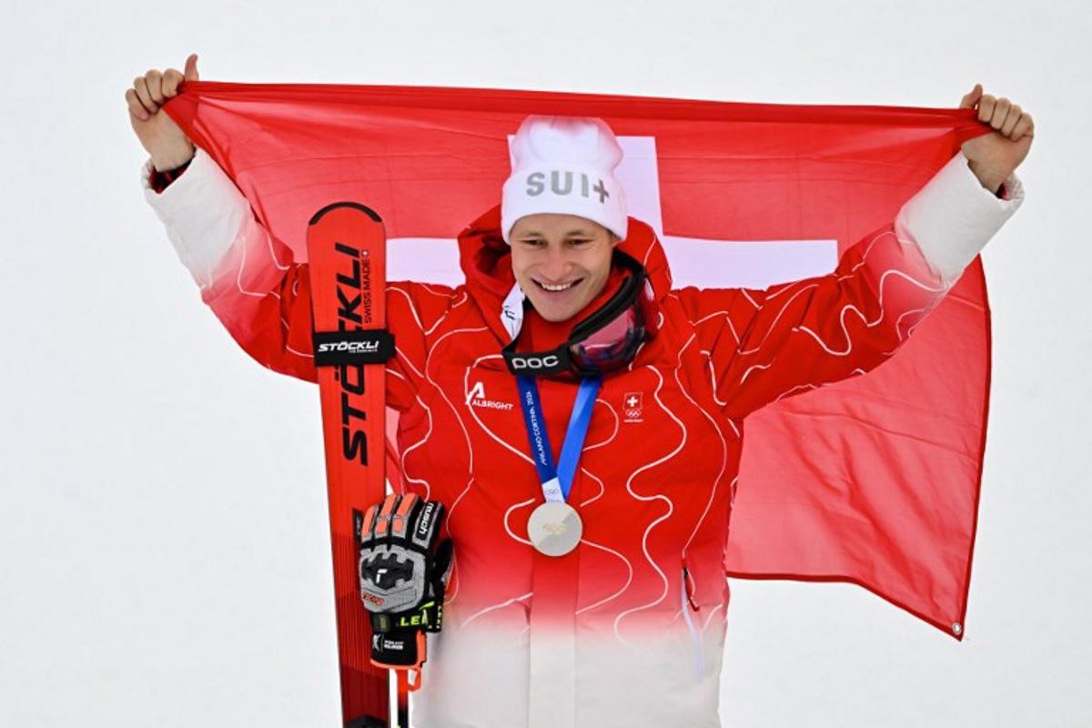 Switzerland's silver medalist Marco Odermatt holds up a Swiss flag after the men's giant slalom alpine skiing event during the Milano Cortina 2026 Winter Olympic Games at the Stelvio Ski Centre in Bormio (Valtellina) on February 14, 2026.  Fabrice COFFRINI / AFP