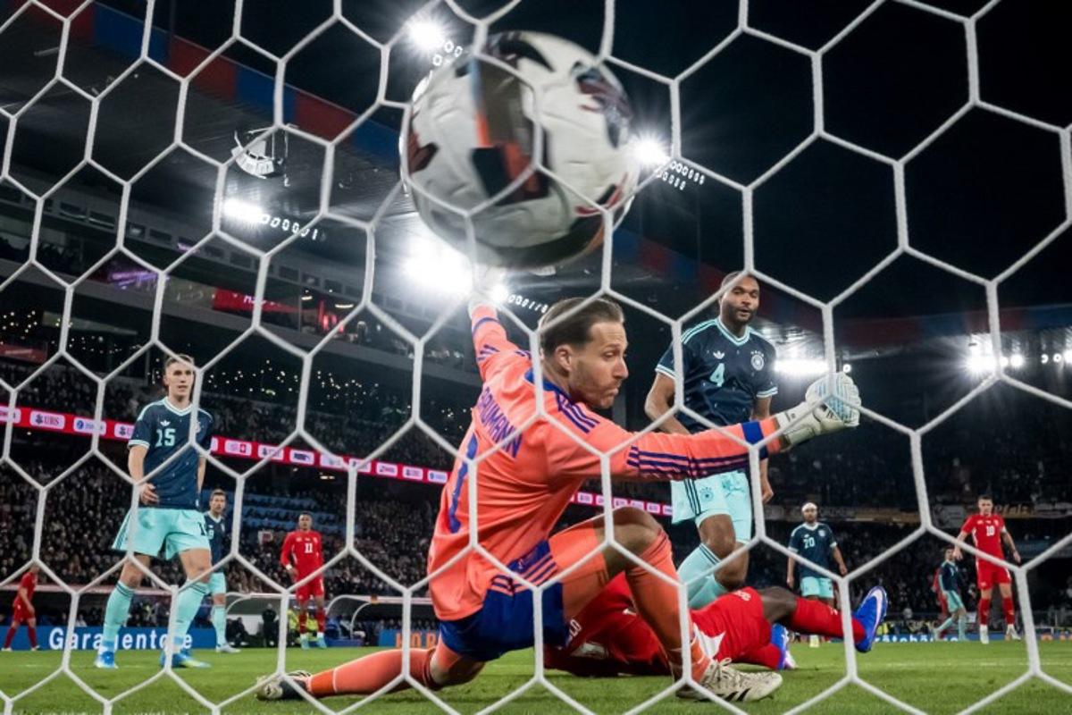 Switzerland's forward #7 Breel Embolo (Bottom) scores his team's second goal past Germany's goalkeeper #01 Oliver Baumann and Germany's defender #04 Jonathan Tah during the international friendly football match between Switzerland and Germany at St. Jakob-Park in Basel, Switzerland on March 27, 2026.  Fabrice COFFRINI / AFP