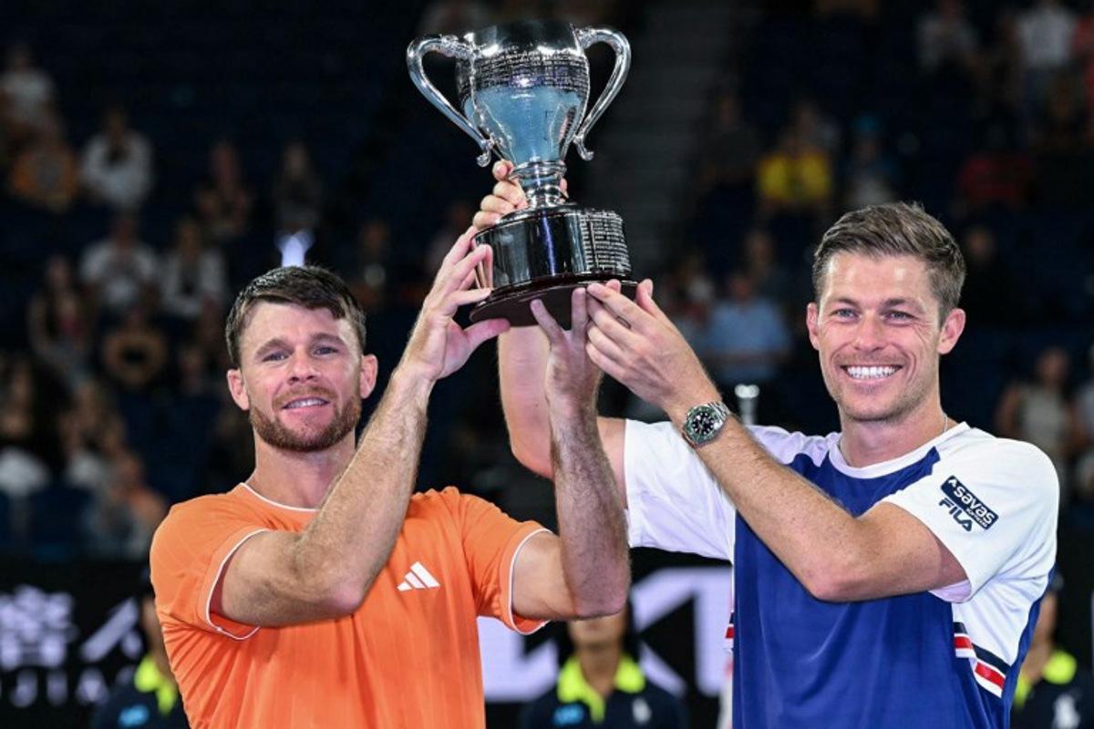 Great Britain's Neal Skupski (R) and his partner USA's Christian Harrison celebrate with the trophy after winning their men's doubles final match against Australia's Jason Kubler and Marc Polmans on day fourteen of the Australian Open tennis tournament in Melbourne on January 31, 2026.  WILLIAM WEST / AFP