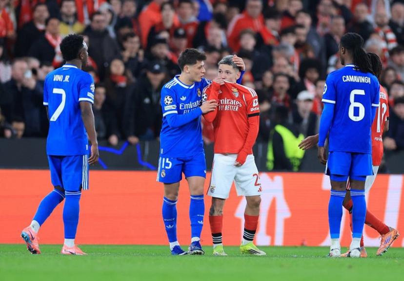 SL Benfica's Argentine forward #25 Gianluca Prestianni hides his mouth while arguing with Real Madrid's Brazilian forward #07 Vinicius Junior who complained about alleged racists insults during the UEFA Champions League knockout round play-off first leg football match between SL Benfica and Real Madrid CF at Estadio da Luz in Lisbon on February 17, 2026.  PATRICIA DE MELO MOREIRA / AFP