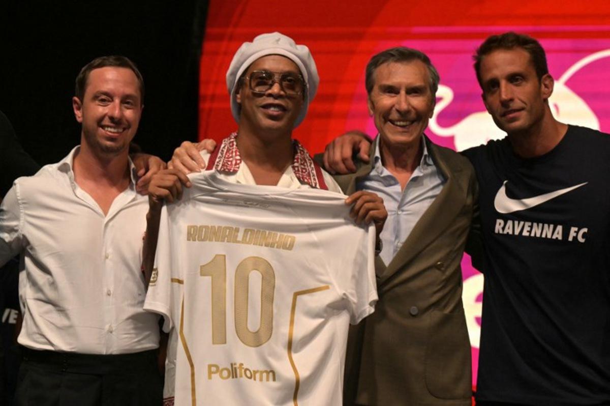 Newly recruited Brazilian football player Ronaldinho poses on stage with the jersey of Ravenna FC next to the president of the club, Ignazio Cipriani (R) during the team presentation in Marina di Ravenna on August 20, 2026.  Former Ballon d'Or and World Cup winner Ronaldinho is set to come out of retirement aged 46 to play for Ravenna in the Italian third tier. Stefano RELLANDINI / AFP