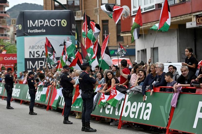 Police officers stand as Pro-Palestinian demonstrators wave Palestinian flags at the finish line of the 12th stage of the Vuelta a Espana, a 144,9 km race between Laredo and Corrales de Buelna, on September 4, 2025.   ANDER GILLENEA / AFP