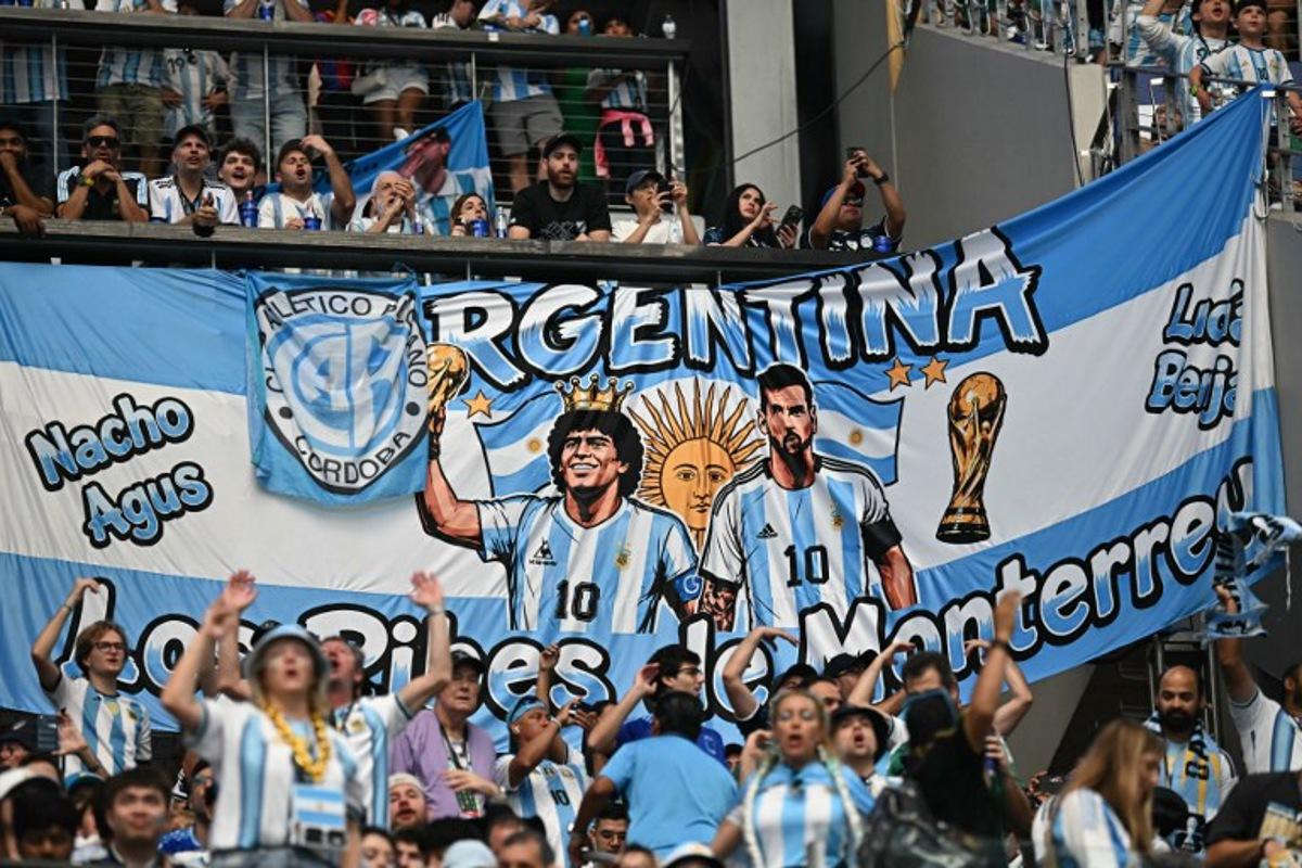 Argentina supporters cheer in front of a banner depicting late Argentine football player Diego Maradona and Argentina's forward #10 Lionel Messi during the 2026 World Cup Group J football match between Argentina and Austria at the Dallas Stadium in Arlington on June 22, 2026. Paul ELLIS / AFP