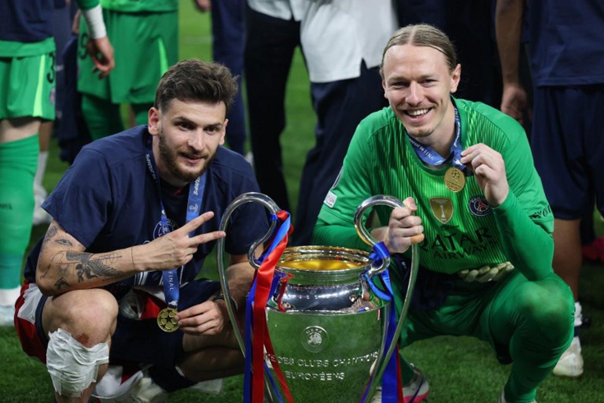 Paris Saint-Germain's Georgian forward #07 Khvicha Kvaratskhelia (L) and Paris Saint-Germain's Russian goalkeeper #39 Matvey Safonov pose with the trophy after winning the UEFA Champions League final football match between Paris Saint-Germain (PSG) and Arsenal FC at the Puskas Arena in Budapest on May 30, 2026. FRANCK FIFE / AFP