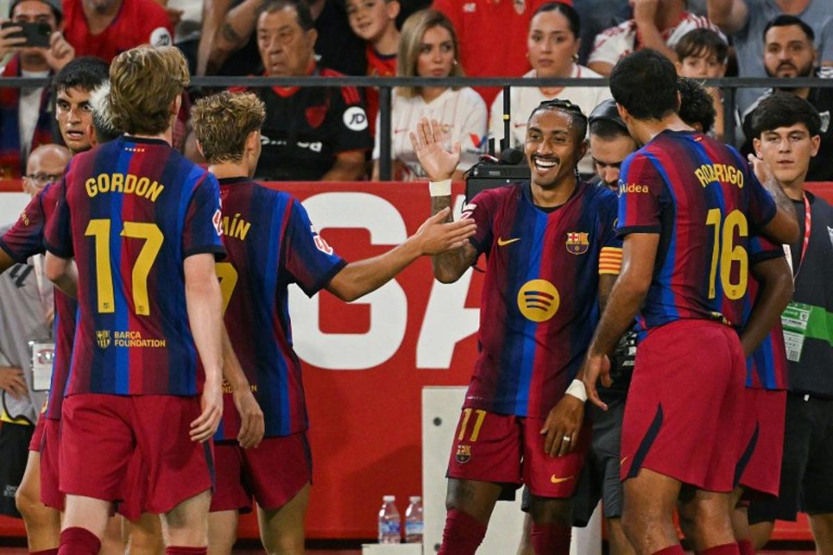 Barcelona's Brazilian forward #11 Raphinha (C) celebrates with teammates after scoring his team's third goal during the Spanish league football match between Sevilla FC and FC Barcelona at the Ramon Sanchez Pizjuan stadium in Seville on September 19, 2026. JORGE GUERRERO / AFP