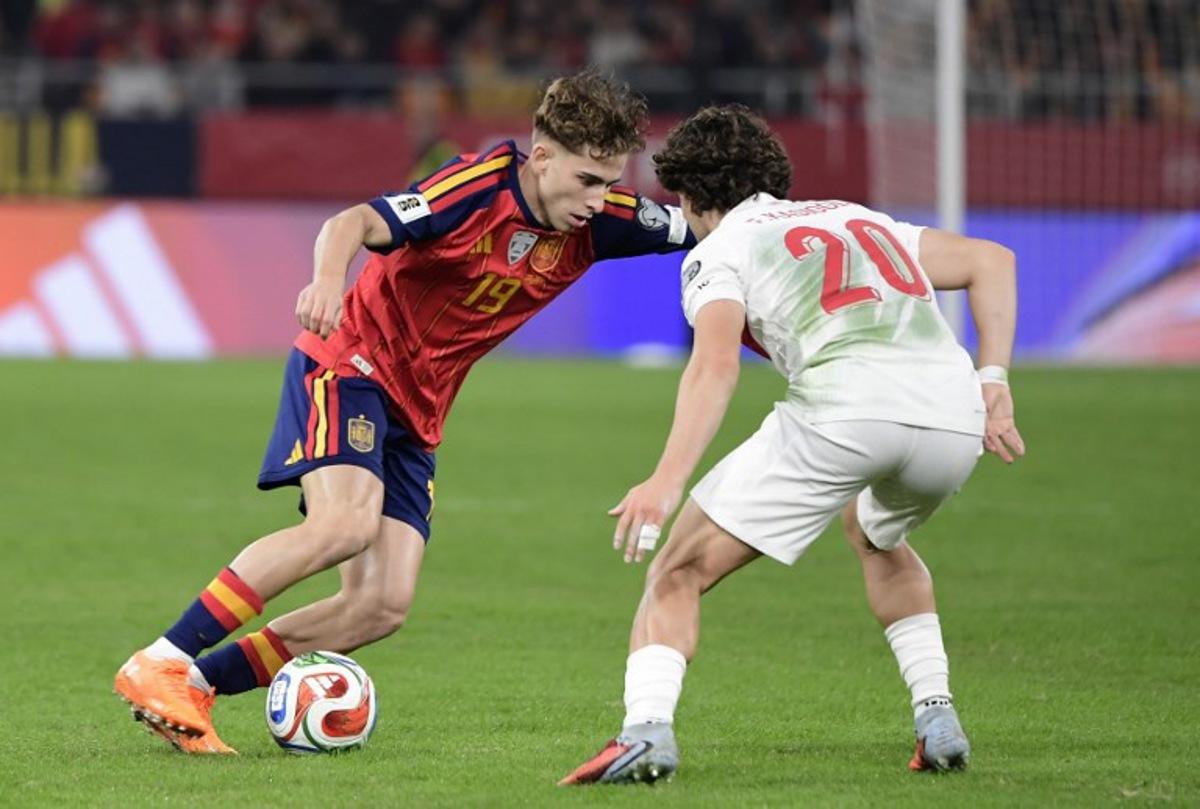 Spain's forward #19 Fermin Lopez fights for the ball with Turkey's defender #20 Ferdi Kadioglu during the FIFA World Cup 2026 European qualification Group E football match between Spain and Turkey at the Cartuja stadium in Seville on November 18, 2025. CRISTINA QUICLER / AFP