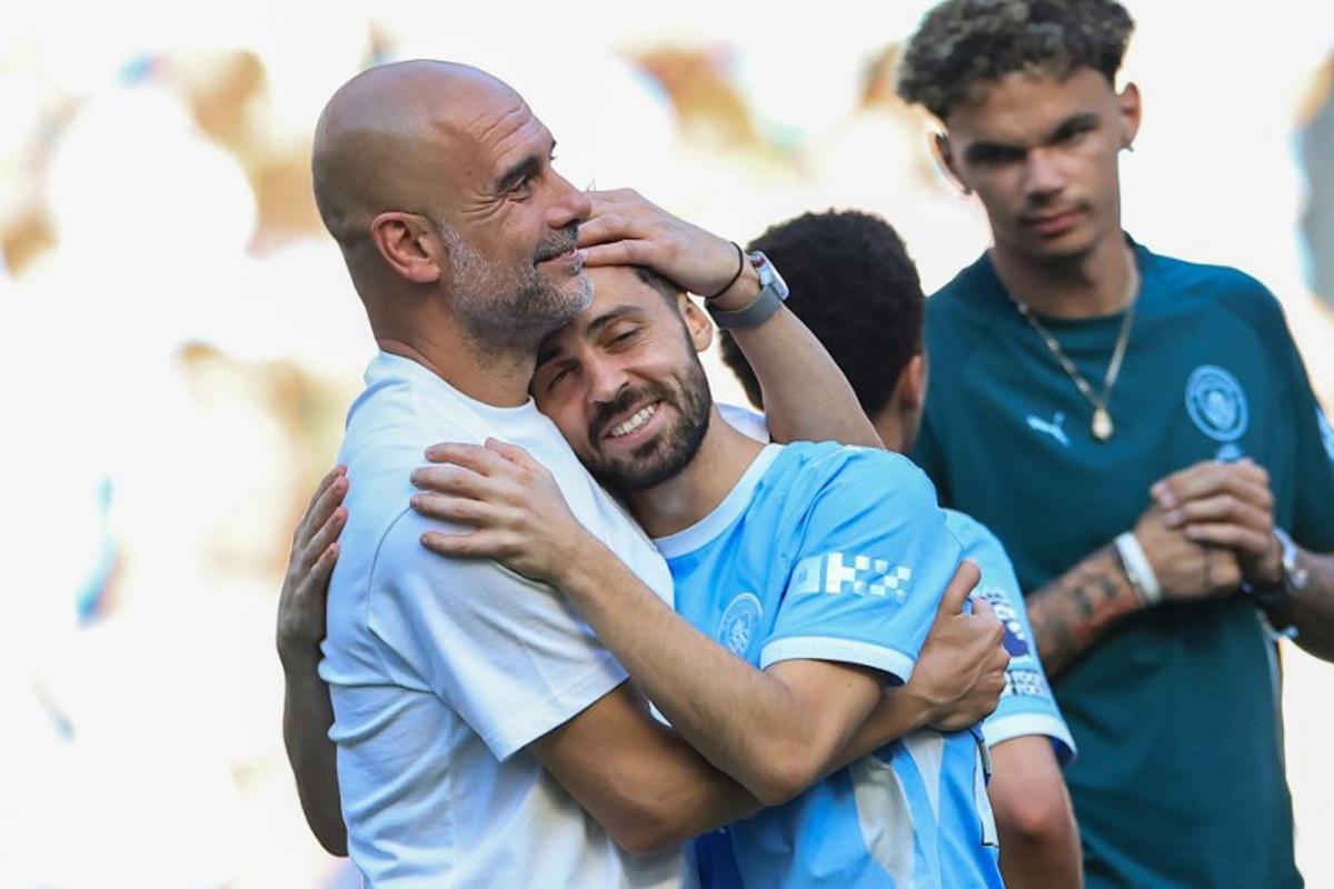 Manchester City's Spanish manager Pep Guardiola (L) embraces Manchester City's Portuguese midfielder #20 Bernardo Silva (C) during ceremonies following the English Premier League football match between Manchester City and Aston Villa at the Etihad Stadium in Manchester, north west England, on May 24, 2026. Darren Staples / AFP