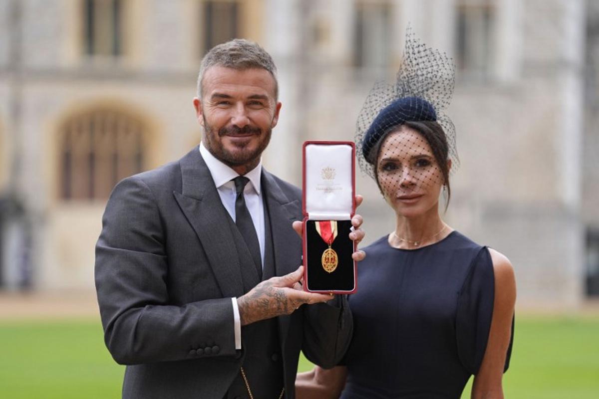 Former England footballer David Beckham (L) poses next to his wife singer and fashion designer Victoria Beckham (R) with his medal after being appointed as a Knight Bachelor (Knighthood) for services to sport and charity at an investiture ceremony at Windsor Castle on November 4, 2025. Andrew Matthews / POOL / AFP