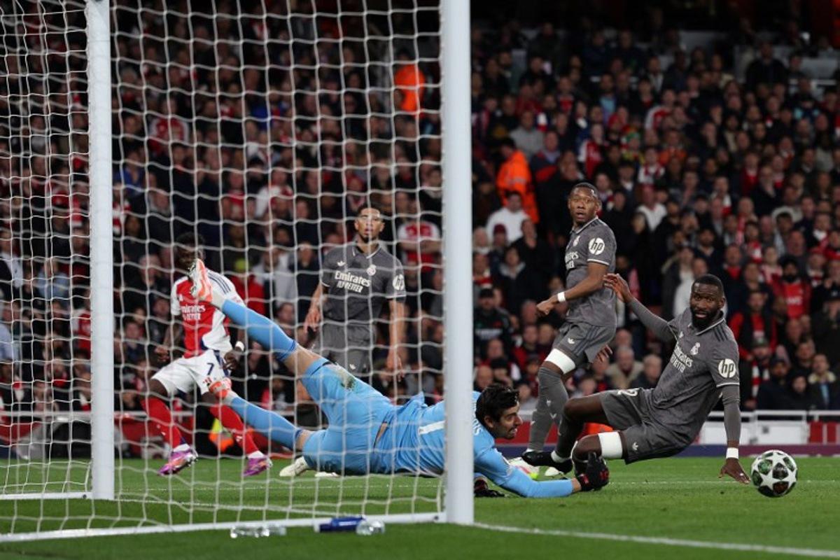 Real Madrid's Belgian goalkeeper #01 Thibaut Courtois saves a shot from Arsenal's English midfielder #07 Bukayo Saka during the UEFA Champions League Quarter final first leg football match between Arsenal and Real Madrid, at the Emirates Stadium, in London, on April 8, 2025. Adrian Dennis / AFP