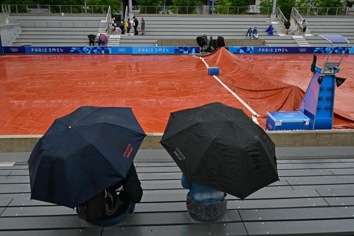 Spectators take shelter from the rain as the wet weather delays the start of play on the outside courts at the Roland-Garros Stadium at the Paris 2024 Olympic Games, in Paris on July 27, 2024. Miguel MEDINA / AFP