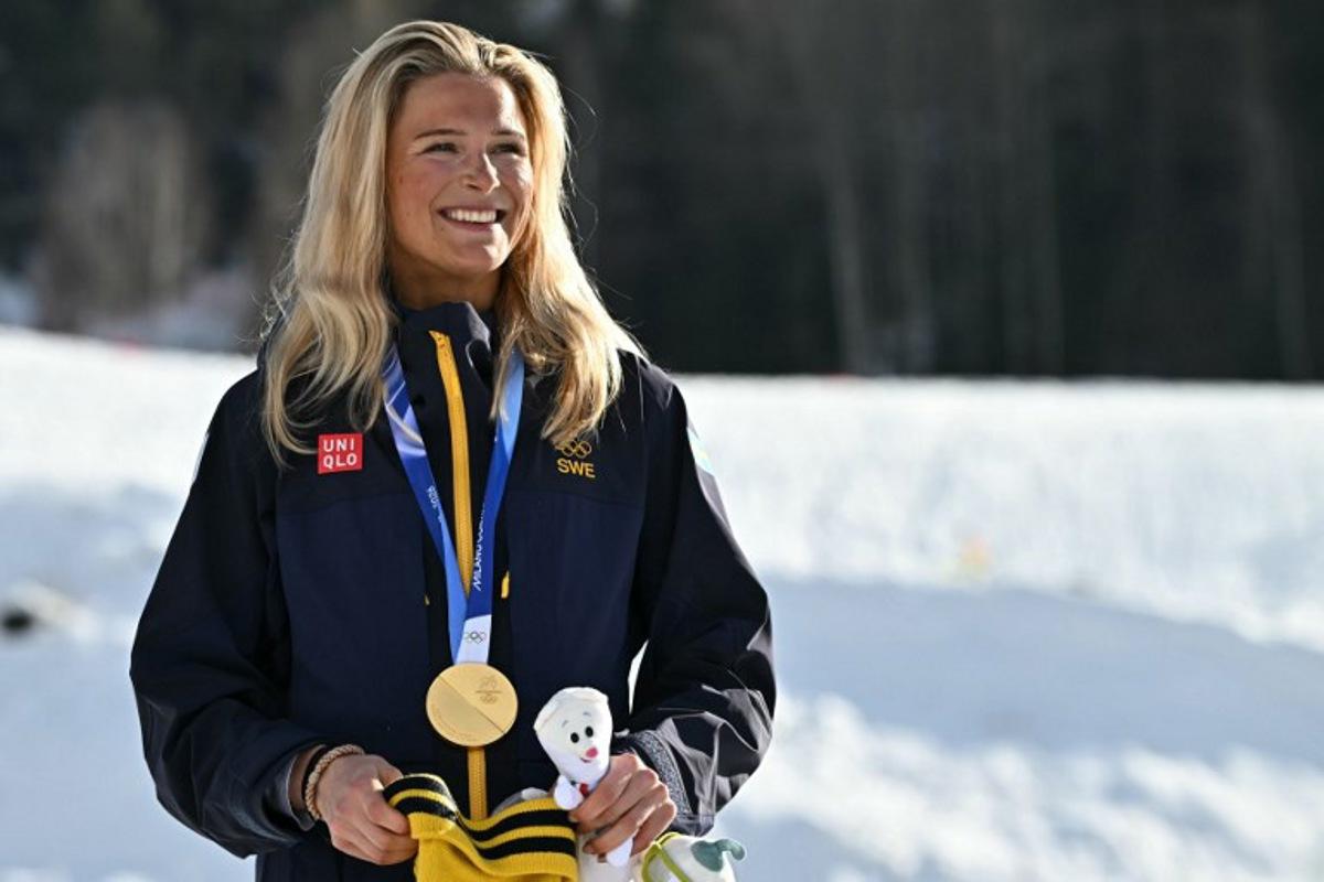 Gold medallist Sweden's Frida Karlsson celebrates on the podium for the women's cross country 10km + 10km skiathlon event of the Milano Cortina 2026 Winter Olympics at Tesero Cross-Country Skiing Stadium in Lago di Tesero (Val di Fiemme) on February 7, 2026. Javier SORIANO / AFP