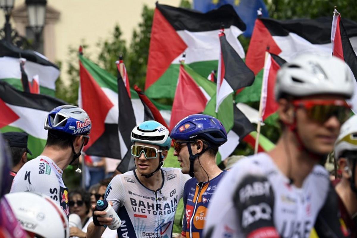 Pro-Palestinian protesters wave flags as riders await the start of the 15th stage of the Vuelta a Espana cycling tour, a 167 km race between A Veiga/Vegadeo and Monforte de Lemos, on September 7, 2025. Miguel RIOPA / AFP